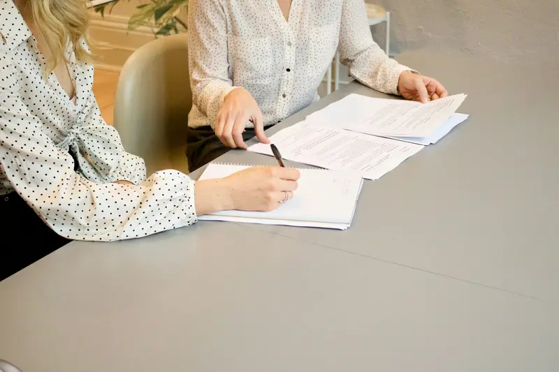 Two people going through and signing paperwork at a desk