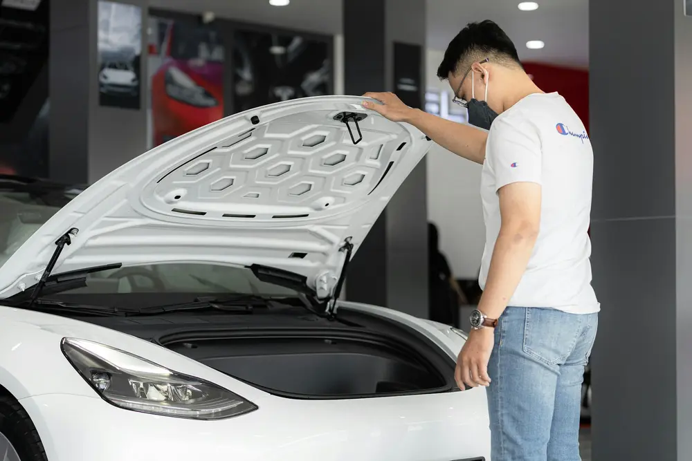 A customer checking a new white car with its bonnet open in a showroom